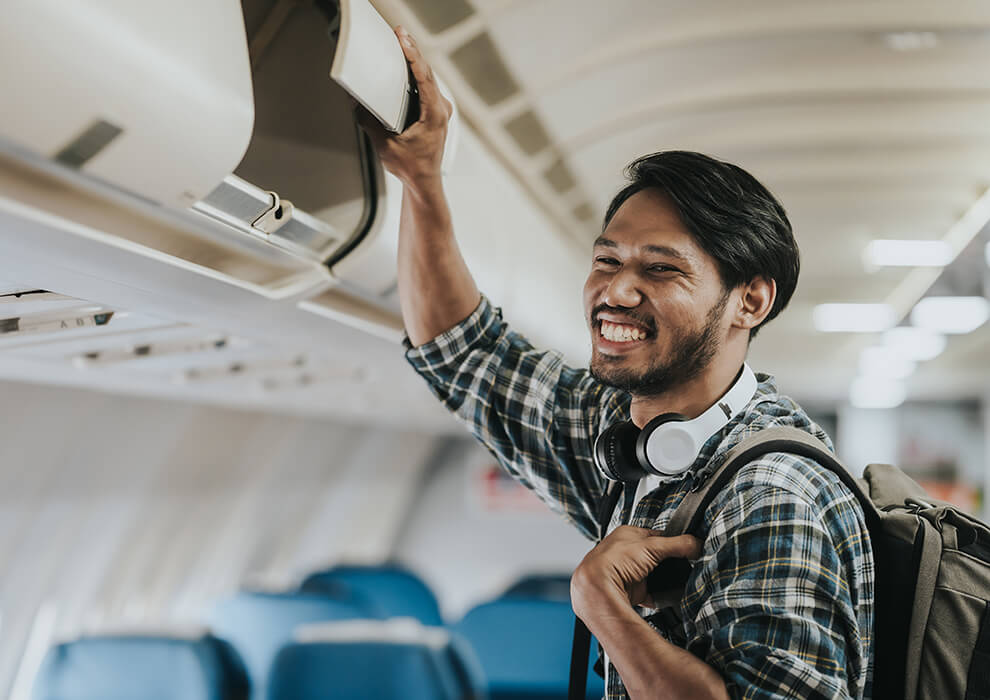 A man puts his luggage in the overhead compartment before his flight